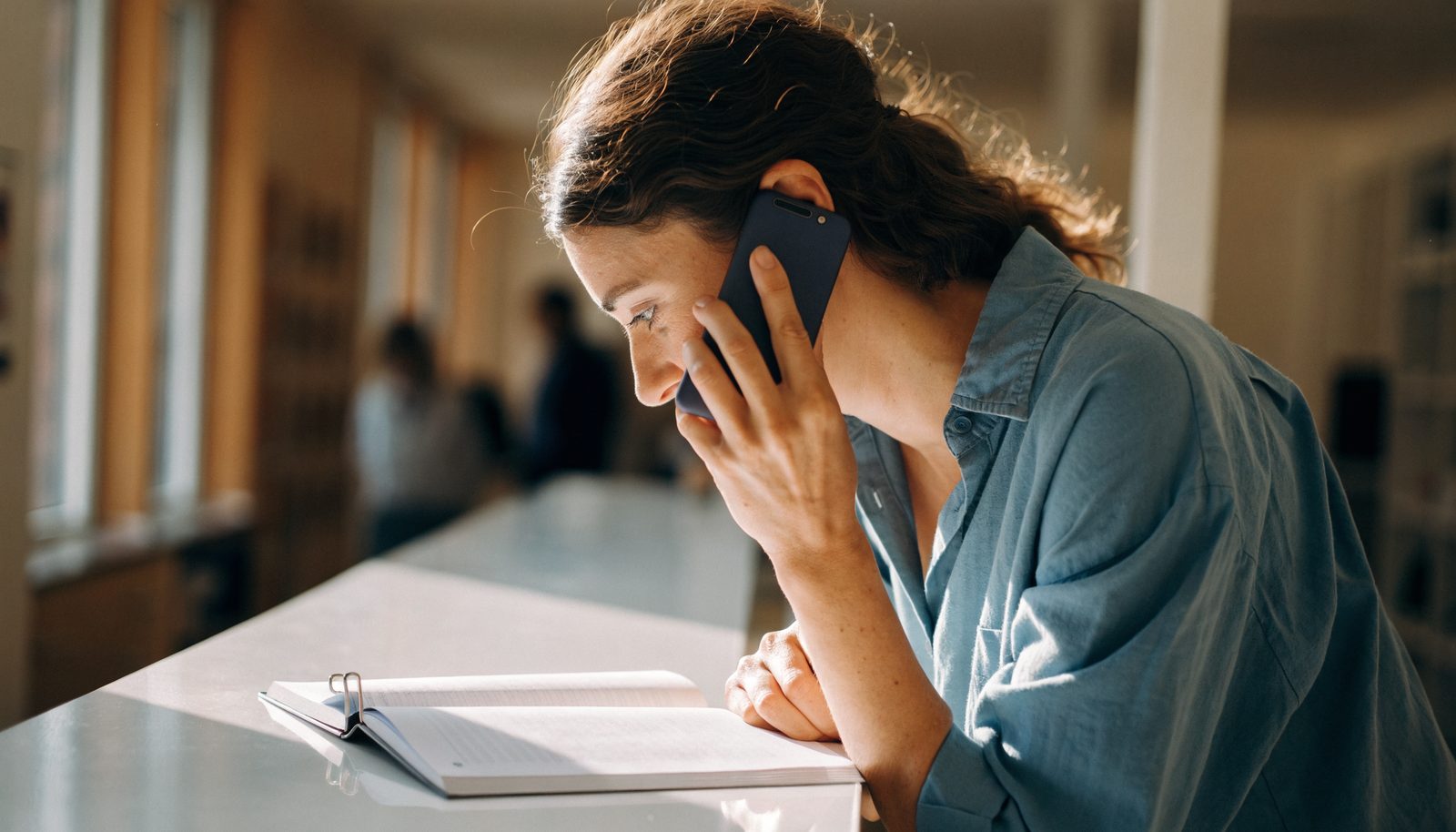 A business owner at a reception counter taking a call, looking down at an open appointment book.